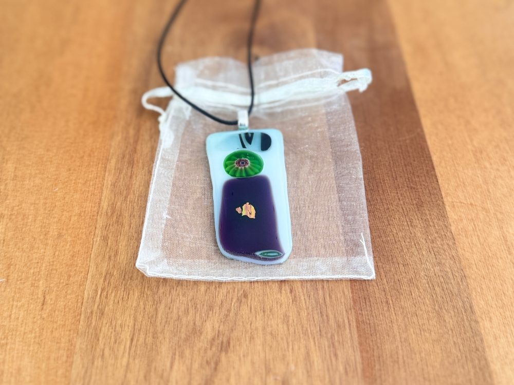 Bloom long fused glass pendant in white and violet glass with a green millefiori flower and dichroic accent, on black cord