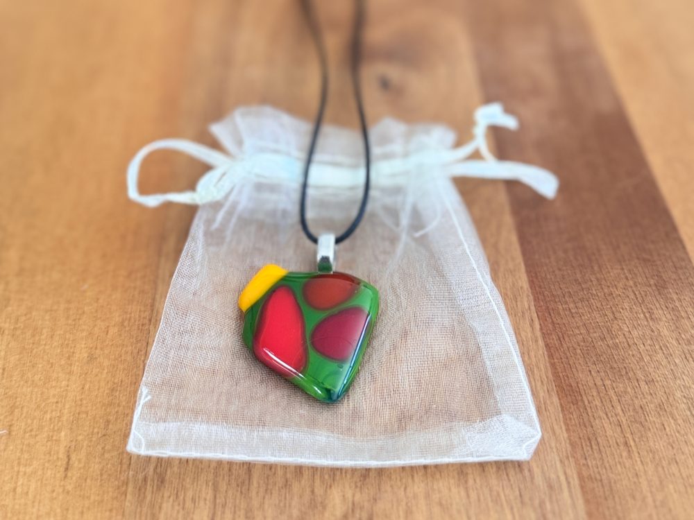 Garden Party fused glass pendant in green glass with red and coral pools and a yellow corner, on black cord